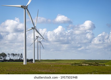 A field with four wind wheels in a row and a blue sky with white clouds