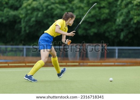 Field hockey female player hit the ball in the game.