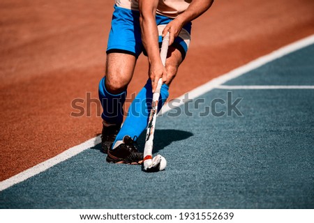 Field hockey player, in possesion of the ball, running over an astroturf pitch, looking for a team mate to pass to. Vintage color filter
