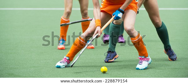 Field hockey players\
challenge eachother for possession of the ball on the midfield\
battle of a hockey mach
