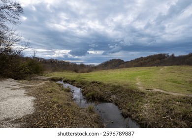 Field with a stream running through it. The sky is cloudy and the grass is dry