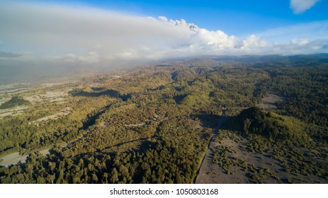 Fields and native forests covered lightly with volcanic ash and in the background the plume of the Calbuco volcano in activity - Powered by Shutterstock