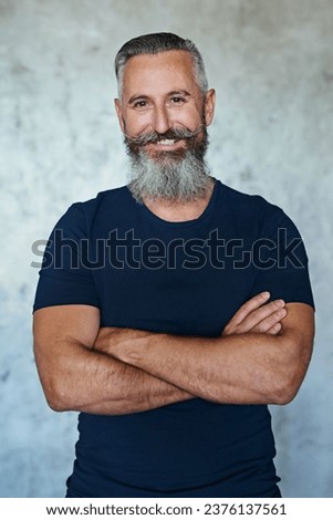 Fierce but always a gentleman. Portrait of a confident middle aged man standing with his arms folded against a grey background.