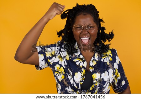 Fierce confident African American dark-haired woman holding fist in front of her as if is ready for fight or challenge, screaming and having aggressive expression on face. 
