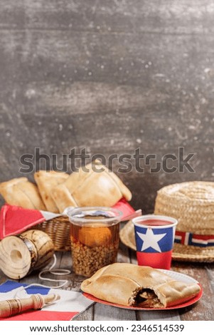 Fiestas Patrias Chile September 18, Independence Day. In vertical. Empanadas, mote con huesillo, chicha or wine, Sombrero huaso chupallas de paja and emboque, on wooden table with flag. copy space