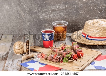 Fiestas Patrias Chile September 18, Independence Day. Anticuchos, mote con huesillo, chicha or wine, Sombrero huaso chupallas de paja and emboque, on a wooden table with a flag. copy space