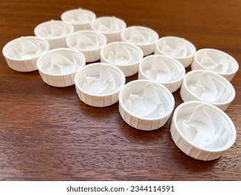 Fifteen white round lids are laid out in a rectangle of three rows of five lids on a brown wooden surface, close-up, side view. Garbage sorting. Caring for the environment. Waste recycling.