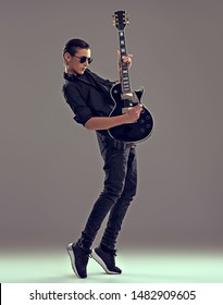 Fifteen Years Old Guitarist With A  Black Electric Guitar. Teenage Musician Holds Guitar, Posing At Studio. The Young Caucasian Guy With A Guitar. Boy's Playing Rock Music. Heavy Metal Player. 