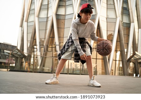 fifteen-year-old teenage asian boy playing basketball outdoors in front of a modern building