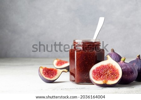 Fig jam in a glass jar on a light gray table. Fruit canning and storage. Jam for cheese and bruschetta. Space for text