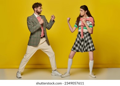 fight, man against woman, young man and woman with clenched fists, opponents, yellow backdrop