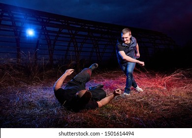 Fight of two men in the field at night time and colored red and blue light around. Special photoshoot about dangerous gangster life in Russia