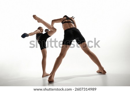 Fighter blocking kick from opponent, intense training moment captured against white studio background. Concept of sport, martial arts, MMA, strength, self-defense, focus, movement, kickboxing, fitness