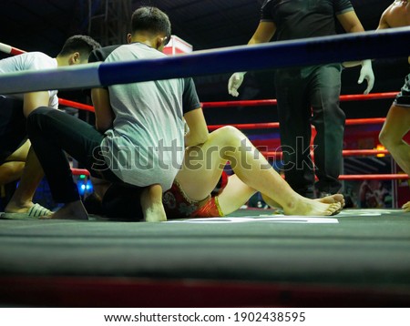 A fighter, boxer, got knocked down on the ring floor, with people in his team quickly get into the boxing ring to urgently help with his breathing
