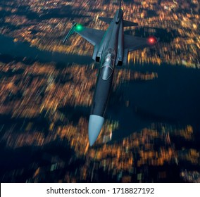 Fighter Jet Aircraft Flying Low Over An Urban Area Of A City In Lights At Night. Army Or Military Bomber Airplane Low Pass Fly By. Aerial Top View