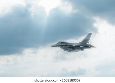 Fighter jet flying through cloudy blue sky on background with copy space