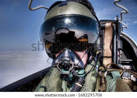 Fighter Pilot in flight wearing flying helmet, dark visor and oxygen mask strapped into ejector seat in flying suit and black visor
