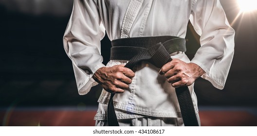 Fighter tightening karate belt against composite image of playing field indoor - Powered by Shutterstock