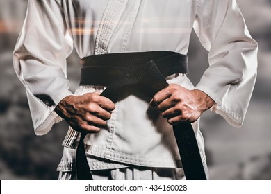 Fighter tightening karate belt against rock crashing down from cliff