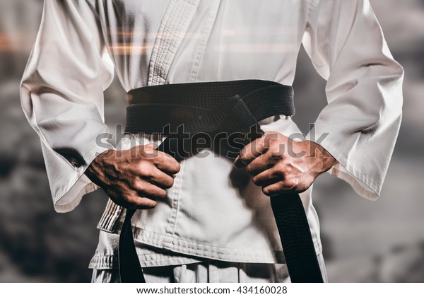 Fighter tightening karate belt against rock\
crashing down from\
cliff