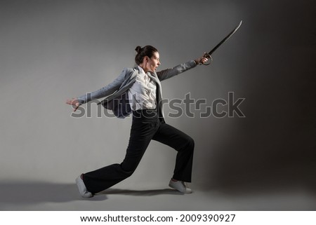 Fighting the invisible enemy in work and career, concept. To overcome self-doubt, a young woman in a suit lunges with a saber in her hands against something in the shadows