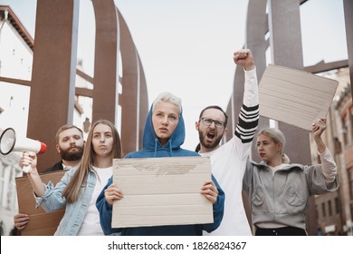 Fighting for more. Group of activists giving slogans in a rally. Caucasian men and women marching together in a protest in the city. Look angry, hopeful, confident. Blank banners for your design or ad - Powered by Shutterstock