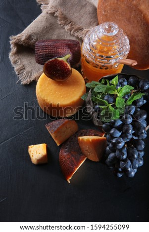 Figs and grapes next to large chunks of hard craft cheese. Photo on black background. The view from the top. Copy space. Vintage tableware.