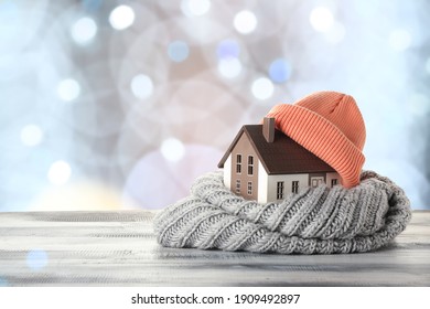 Figure of house and warm clothes on table against blurred lights. Concept of heating season