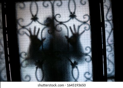 Figure Of Mysterious Stranger Pressing Hands Against A Textured Glass Door With Security Bars