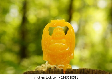 A Figure Of An Orange Buddha Holding A Gold Bar In His Hands.