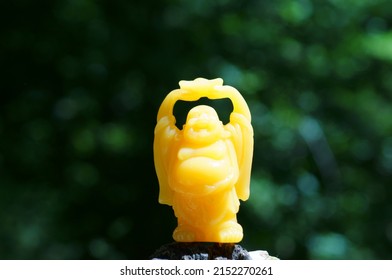 A Figure Of An Orange Buddha Holding A Gold Bar In His Hands.