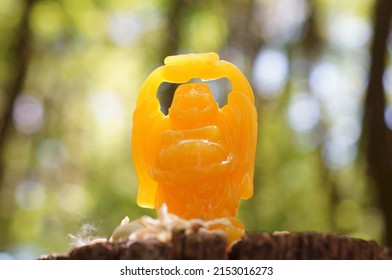 A Figure Of An Orange Buddha Holding A Gold Bar In His Hands.