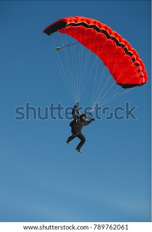 Figure of a parachutist with a bright red parachute against a blue sky.