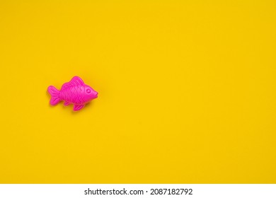 Figure Of Plastic Fish On A Yellow Background With Copy Space. Flat Lay Pink Fish On A Colored Background. Healthy Eating Concept. Baby Toys Concept.