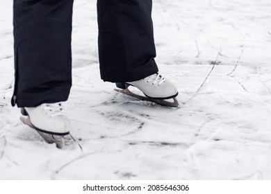 Figure Skating Skates. Close-up Of Man's Legs In Black Winter Pants Standing On Ice Of Frozen Lake In White Figure Skating Skates.