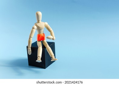 The figure of a wooden man sitting on a dark podium. The figure of a wooden man with a red belly on a blue background. The concept of abdominal diseases and poor health