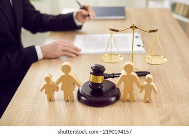 Figures of family are separated by judge's gavel, which symbolizes divorce case and custody of child. Close up of wooden figurines of people on background of judges and scales of justice. - Shutterstock ID 2190194157