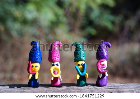 Figures of four fairy-tale dwarfs made of plasticine in the forest on a colored background. The elves have letters in their hands. The inscription love.