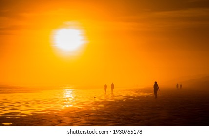 Figures silhouetted on a misty evening. Sunlight dispersed through water vapour illuminating a beach in South Australia.
