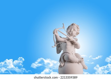 Figurine of an angel Cupid on the podium with a bow and arrow on a blu sky with clouds background . Valentine's Day. - Shutterstock ID 2213359389