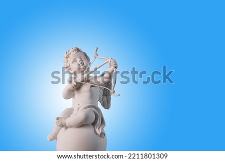 Figurine of an angel Cupid on the podium with a bow and arrow on a blu background . Valentine's Day.Place for text.