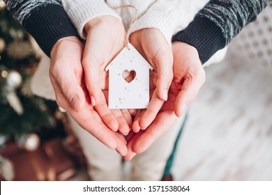 a figurine in the form of a house in which instead of a window the heart. A house in the hands of a man and a woman, a symbol of a young family and their new home