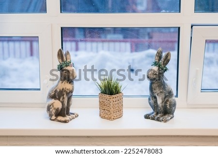 Figurines Easter bunnies and potted grass in the decor of the house window