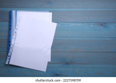 File folder with punched pockets and paper sheets on light blue wooden table, flat lay. Space for text