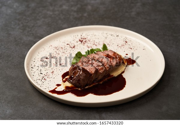 Filet mignon with mashed potatoes\
and pomegranate sauce. Filet mignon Steak with red wine sauce on\
white plate on gray background with copy space,\
close-up