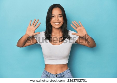 Filipina young woman on blue studio showing number ten with hands.