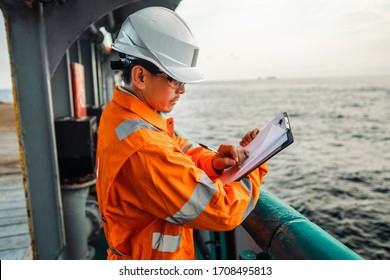 Filipino deck Officer on deck of offshore vessel or ship , wearing PPE personal protective equipment. He fills checklist. Paperwork at sea