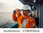 Filipino deck Officer on deck of vessel or ship , wearing PPE personal protective equipment. He is looking through binoculars.