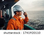 Filipino deck Officer on deck of vessel or ship , wearing PPE personal protective equipment. He speaks to VHF walkie-talkie radio in hands. Dream work at sea