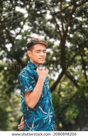 A Filipino man in a blue hawaiian shirt clenches his fist in victory, closing his eyes in relief and bliss.